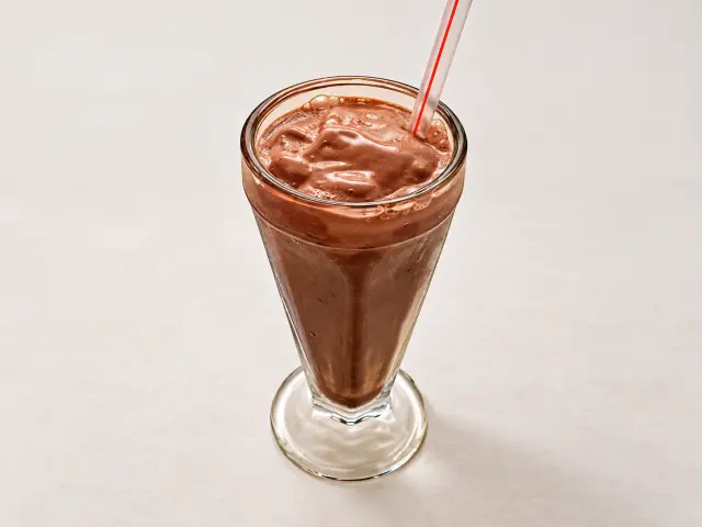 Milk-shake de chocolate servido em taça de vidro com canudo