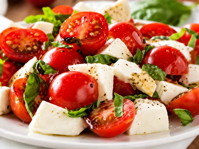 Salada de tomate-cereja com cubos de queijo branco e folhas de manjericão