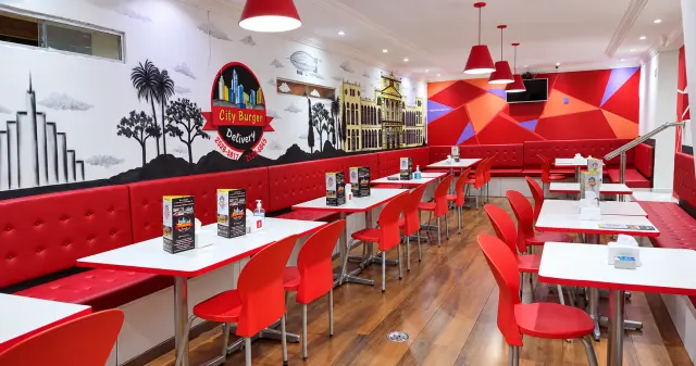 Salão do City Burger com mesas brancas, cadeiras e sofás vermelhos e mural em preto e branco na parede